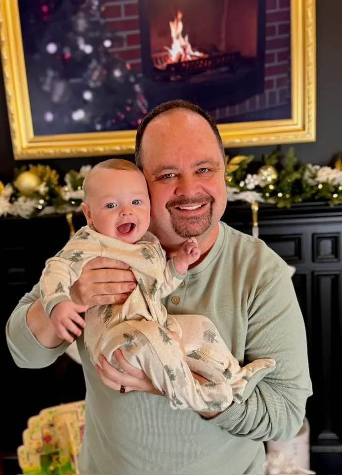 Michael Blair holding a laughing Christian in front of a Christmas mantel