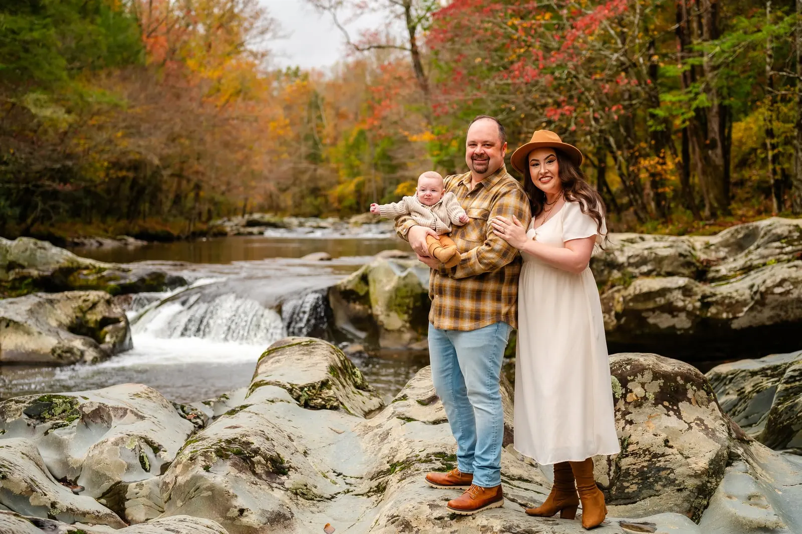Michael Blair holding his son Christian beside his wife Michelle, on the rocks of a mountain creek in fall color